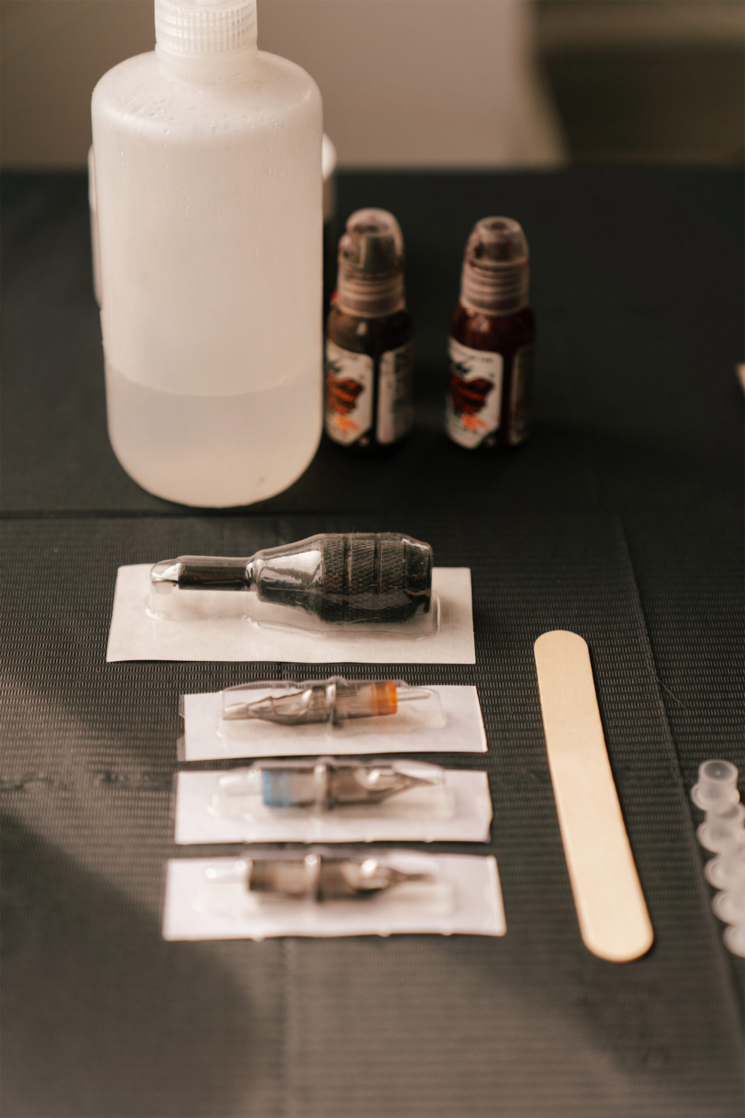 Close-up view of tattoo shop supplies, including tattoo needles, cleaning solutions, wooden sticks, and ink caps.