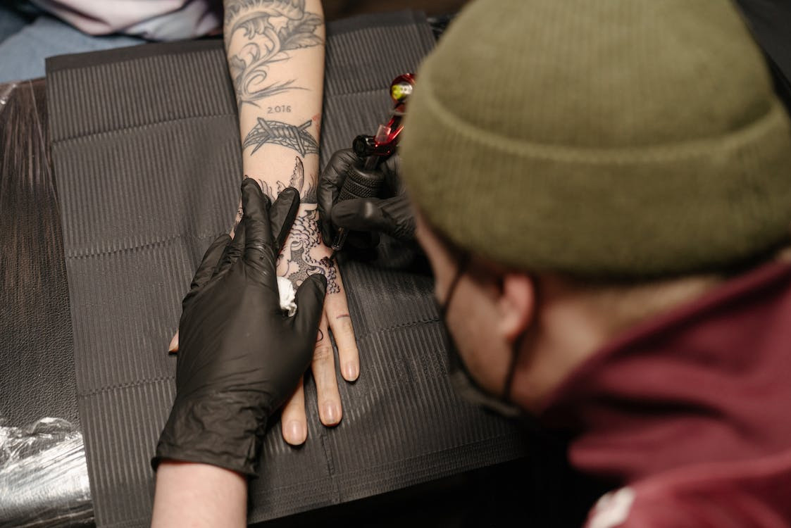 Close-up of a tattoo artist applying a tattoo on a client's arm, using a tattoo machine with precision and care.