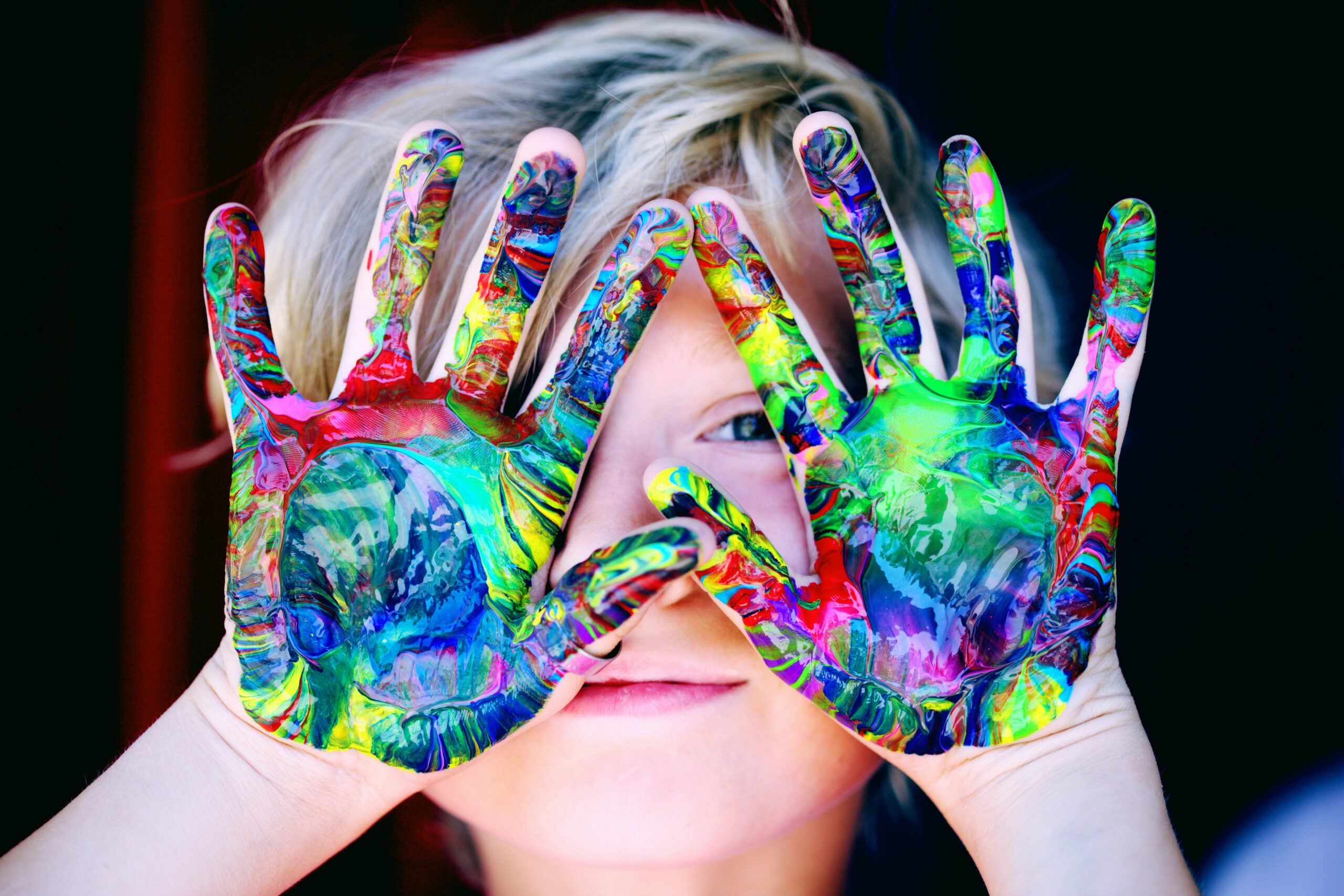 Child with colorful paint-covered hands smiling and showing creativity