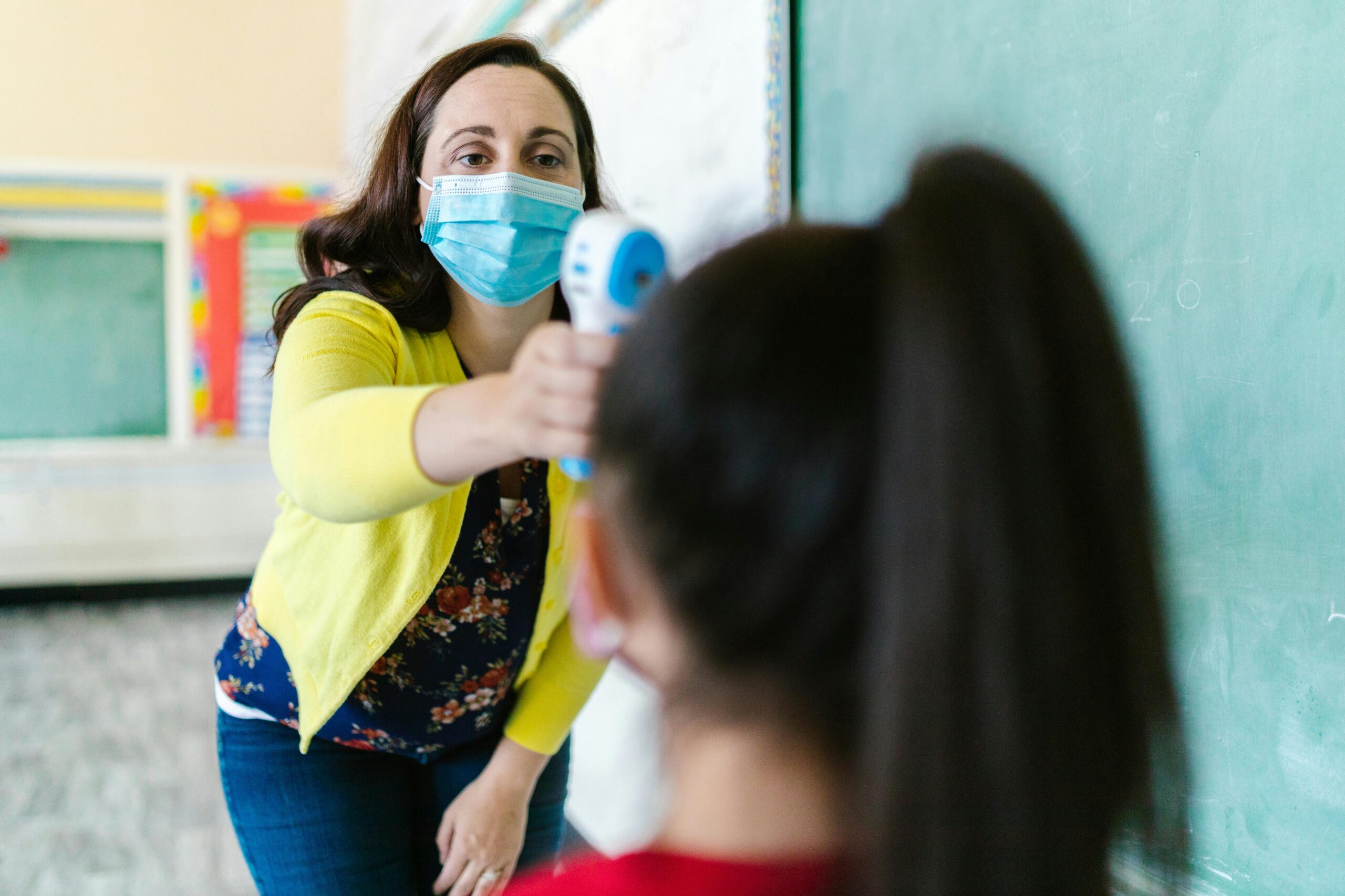 School nurse wearing a mask checking student's temperature with a contactless thermometer