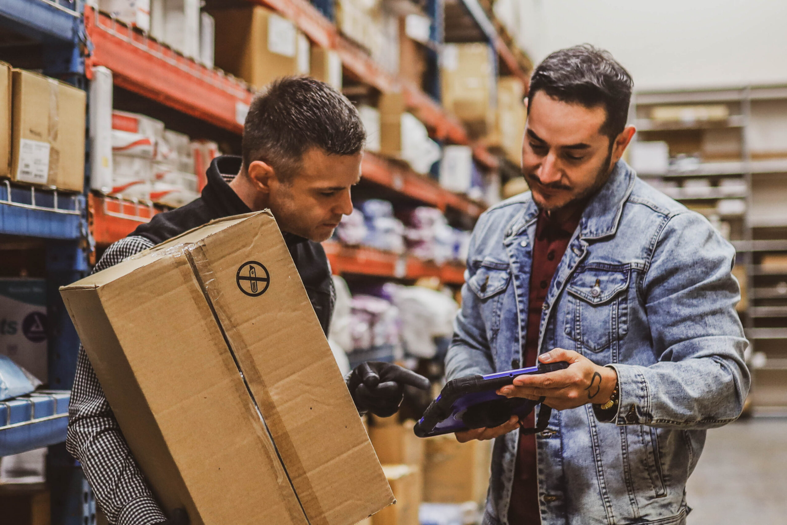 Warehouse workers scanning packages and managing inventory with a tablet device.