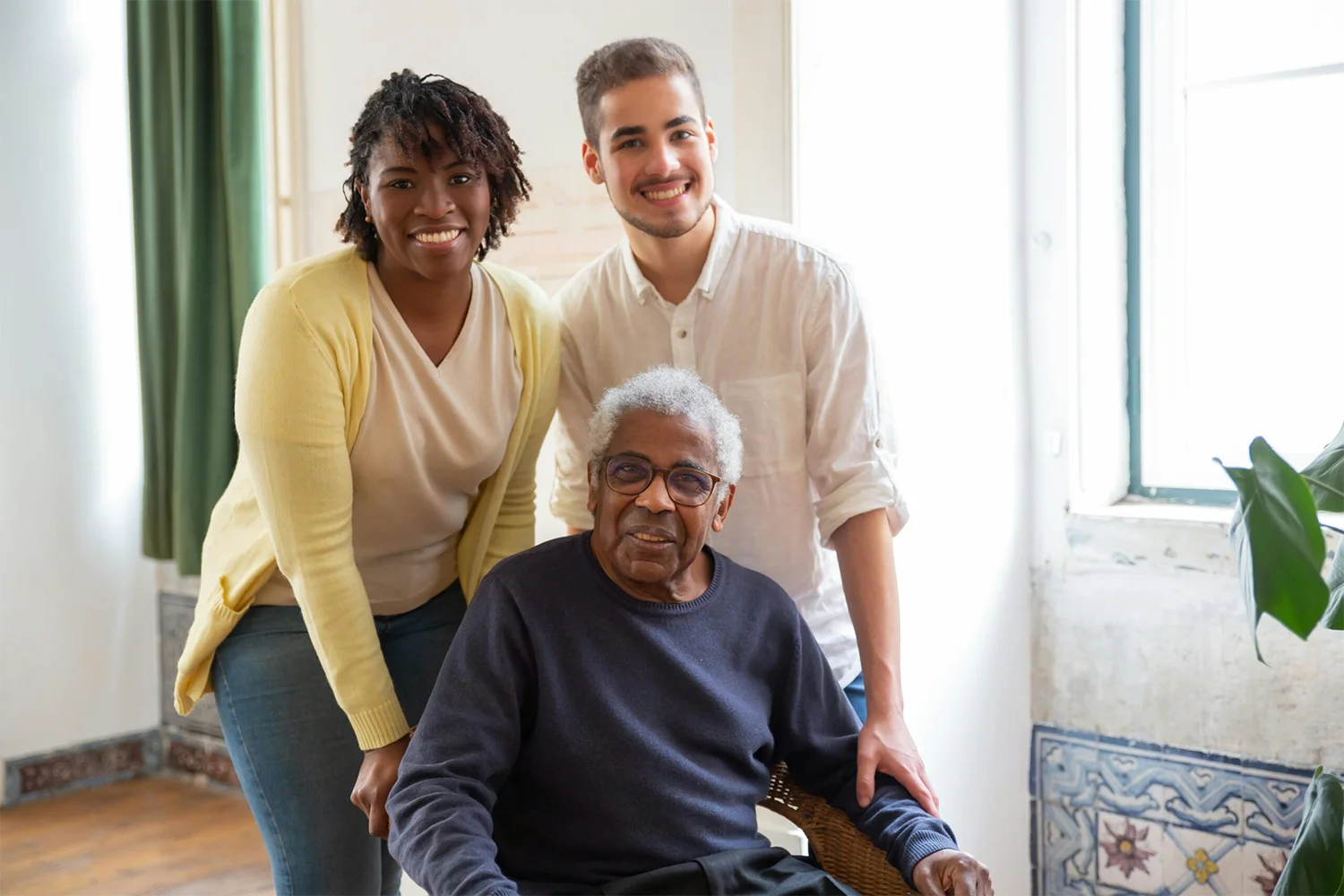 Home health caregivers standing beside an older adult seated in a bright living room.
