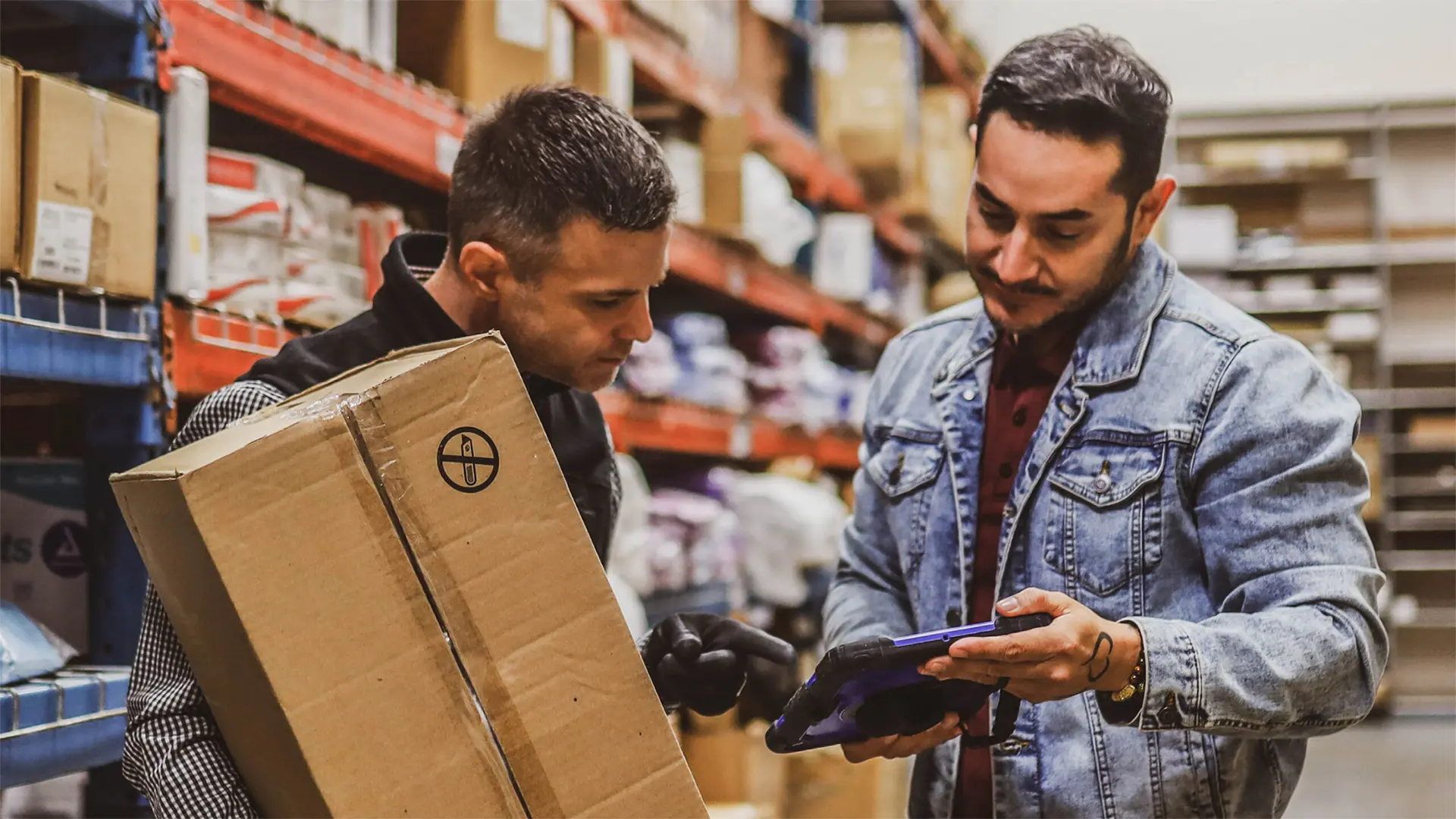 Warehouse workers scanning packages and managing inventory with a tablet device.
