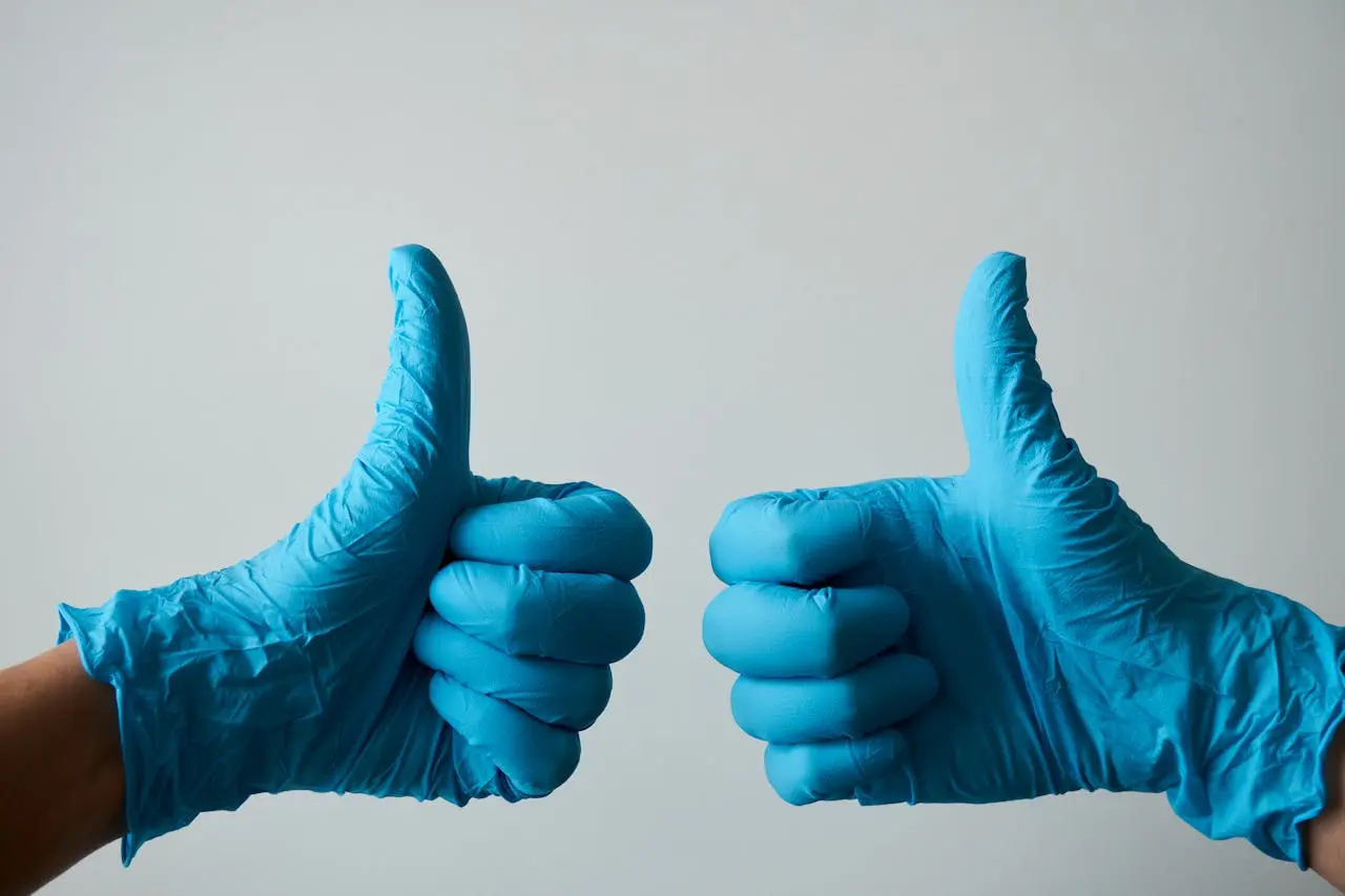Two hands wearing blue medical gloves held up side by side giving thumbs-up gestures